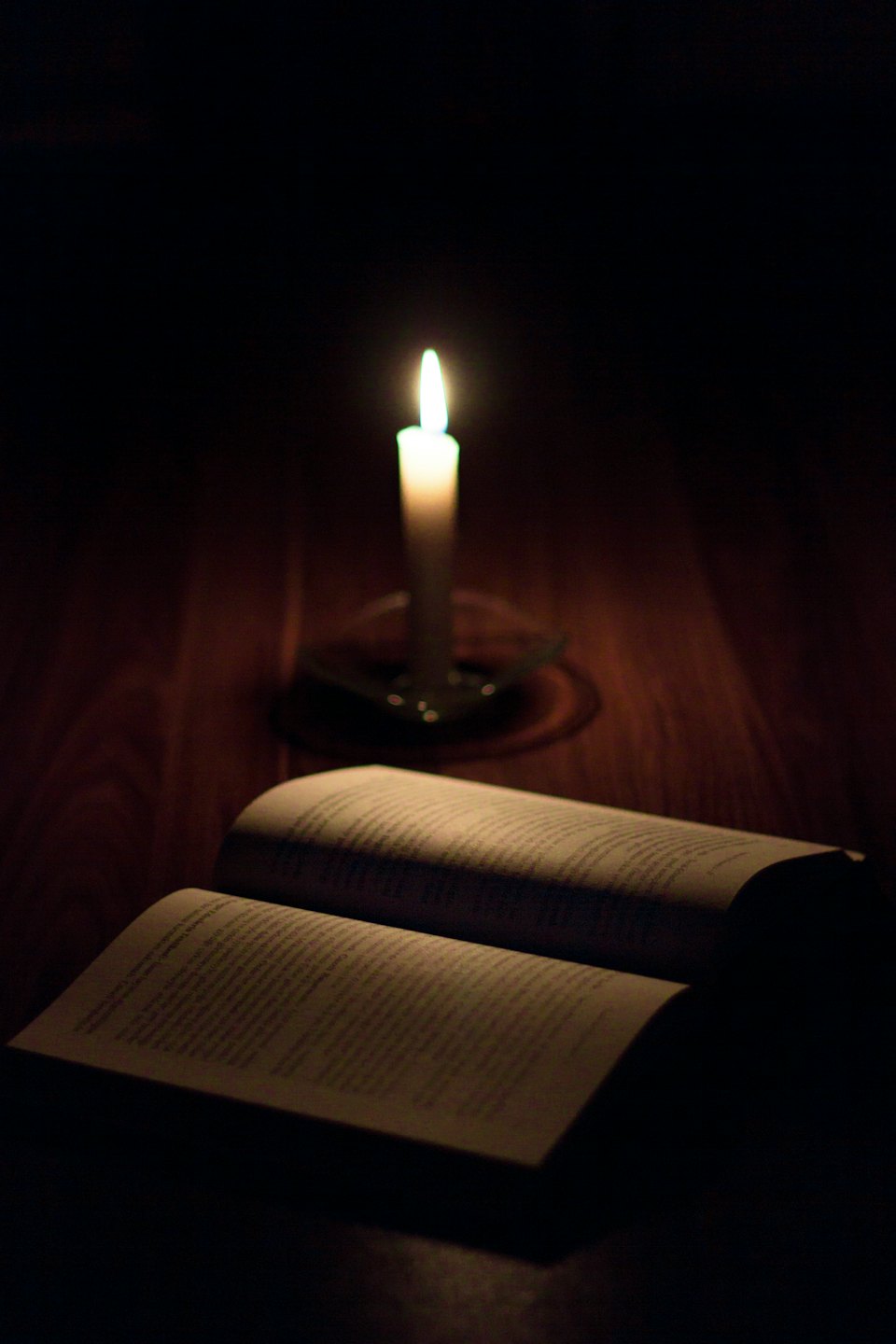 An open book lit by a single burning candle.