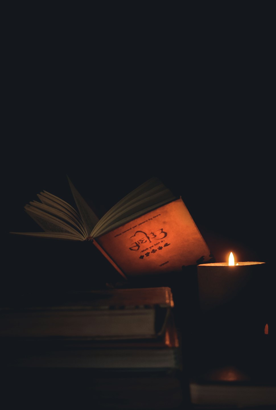 An open antique book sits beside a flickering candle.