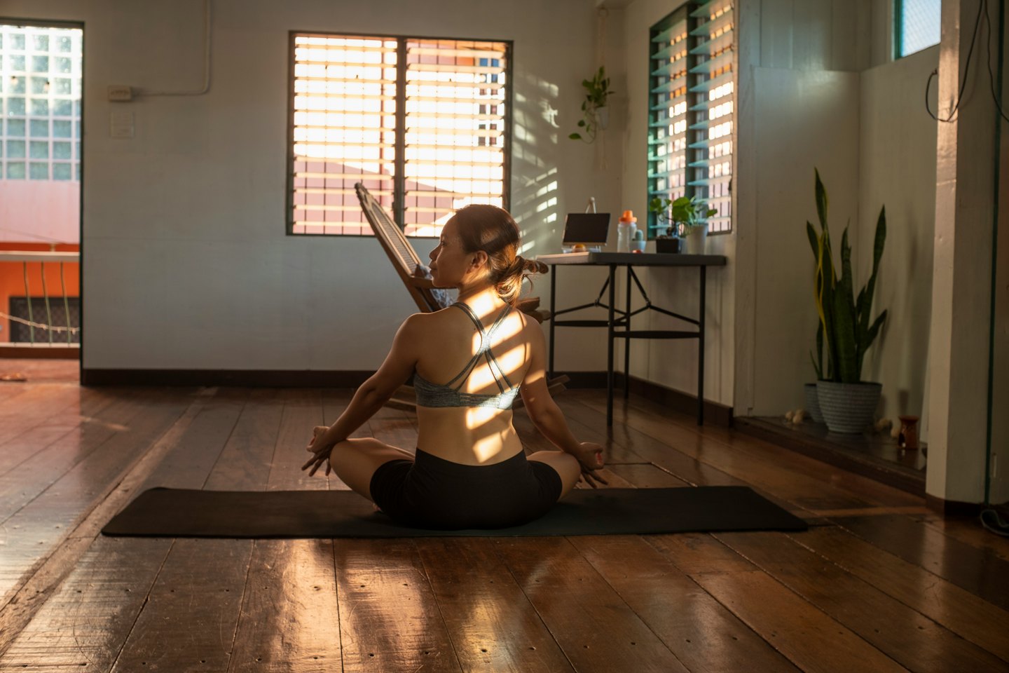 Woman meditates cross-legged on a yoga mat in a sunlit room.